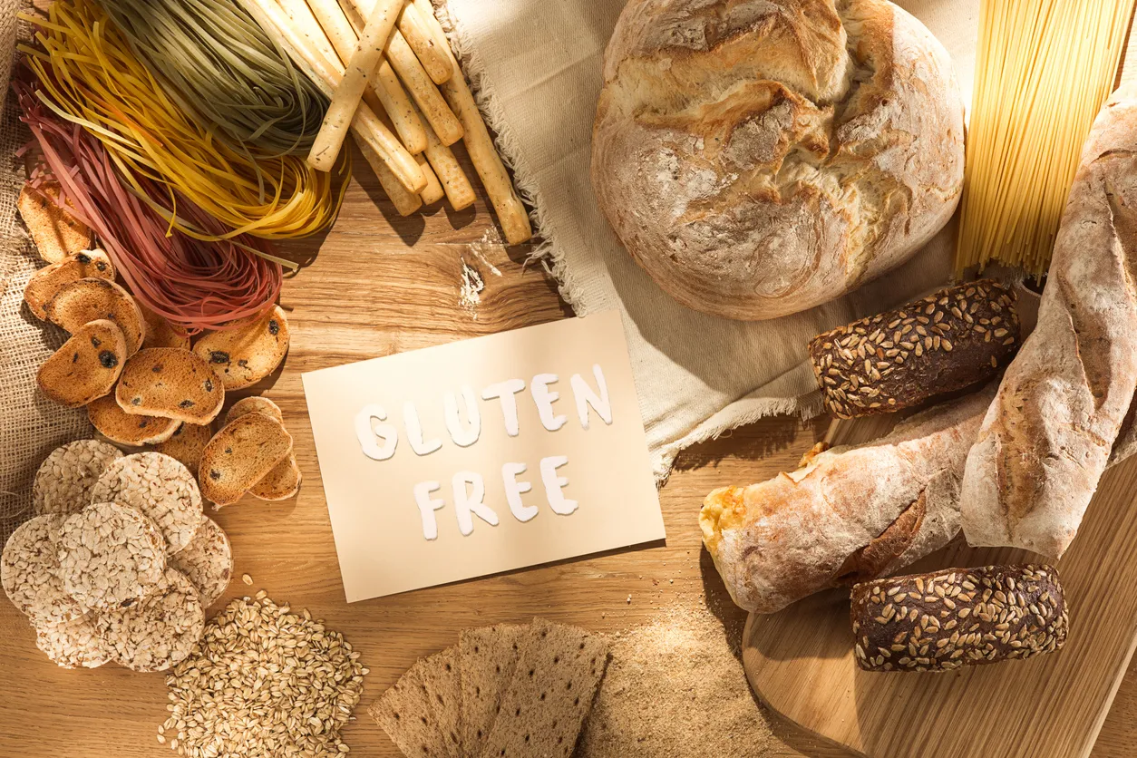 Gluteenittomia tuotteita puupöydällä: leipiä, pastaa, riisikakkuja, kaurahiutaleita ja kyltti jossa lukee Gluten free.